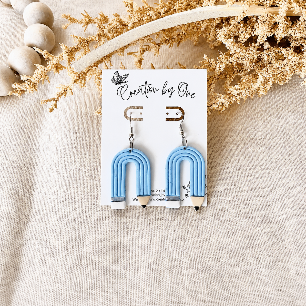 Blue arch-shaped earrings on a 'Creation by One' branded card with decorative elements.