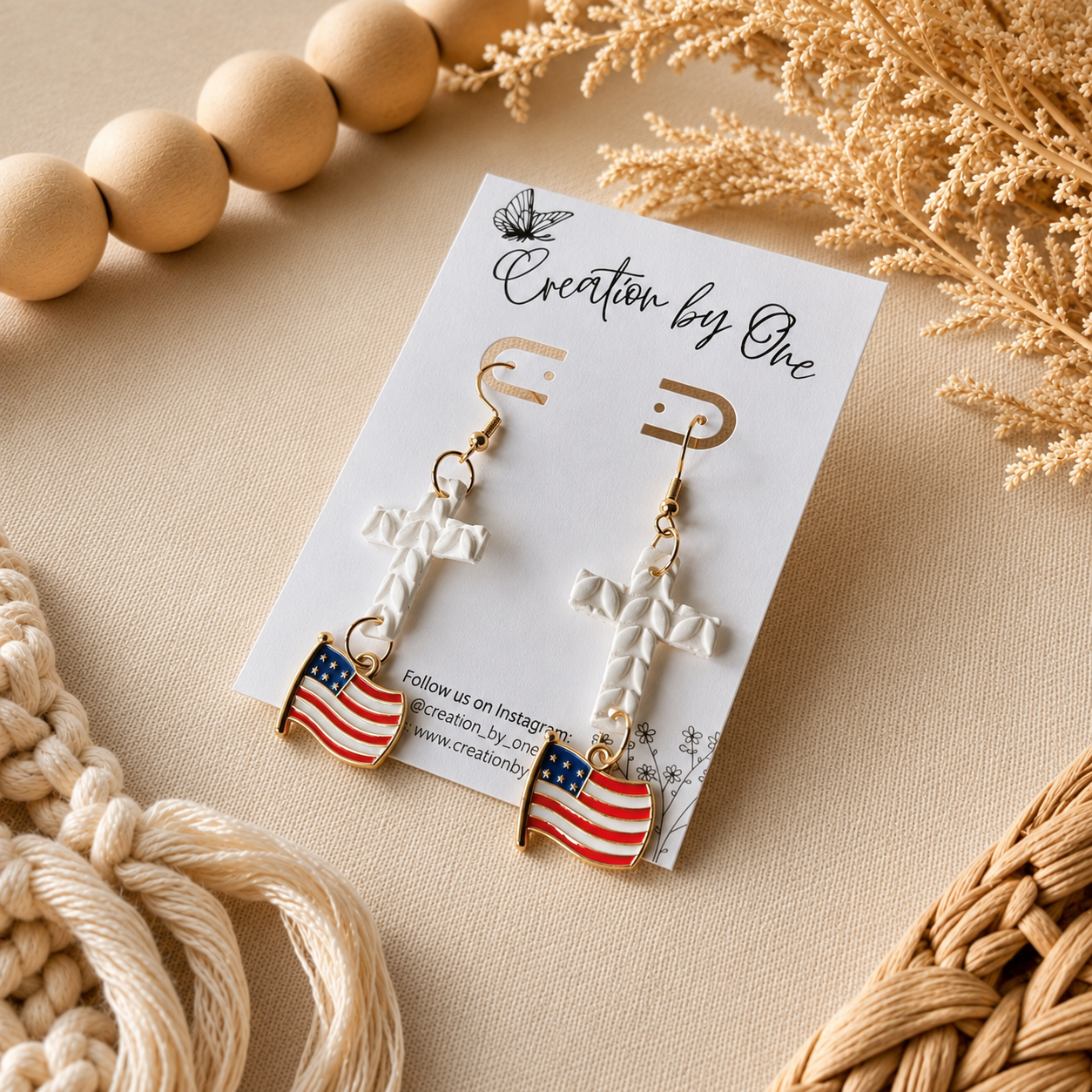 Pair of earrings with American flag design on a 'Creation by One' branded card, surrounded by decorative elements.