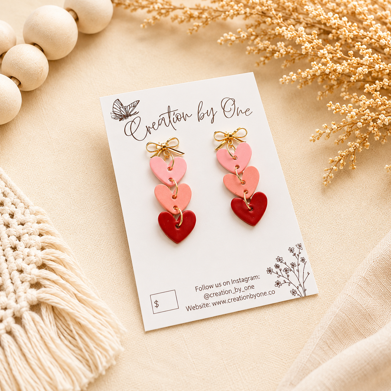 Handmade pink layered heart dangle earrings with gold bow studs on a neutral boho background