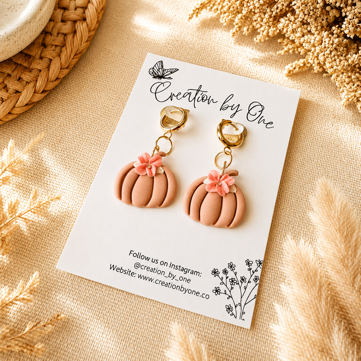 Pair of pink pumpkin-shaped earrings on a 'Creation by One' branded card with dried flowers around.