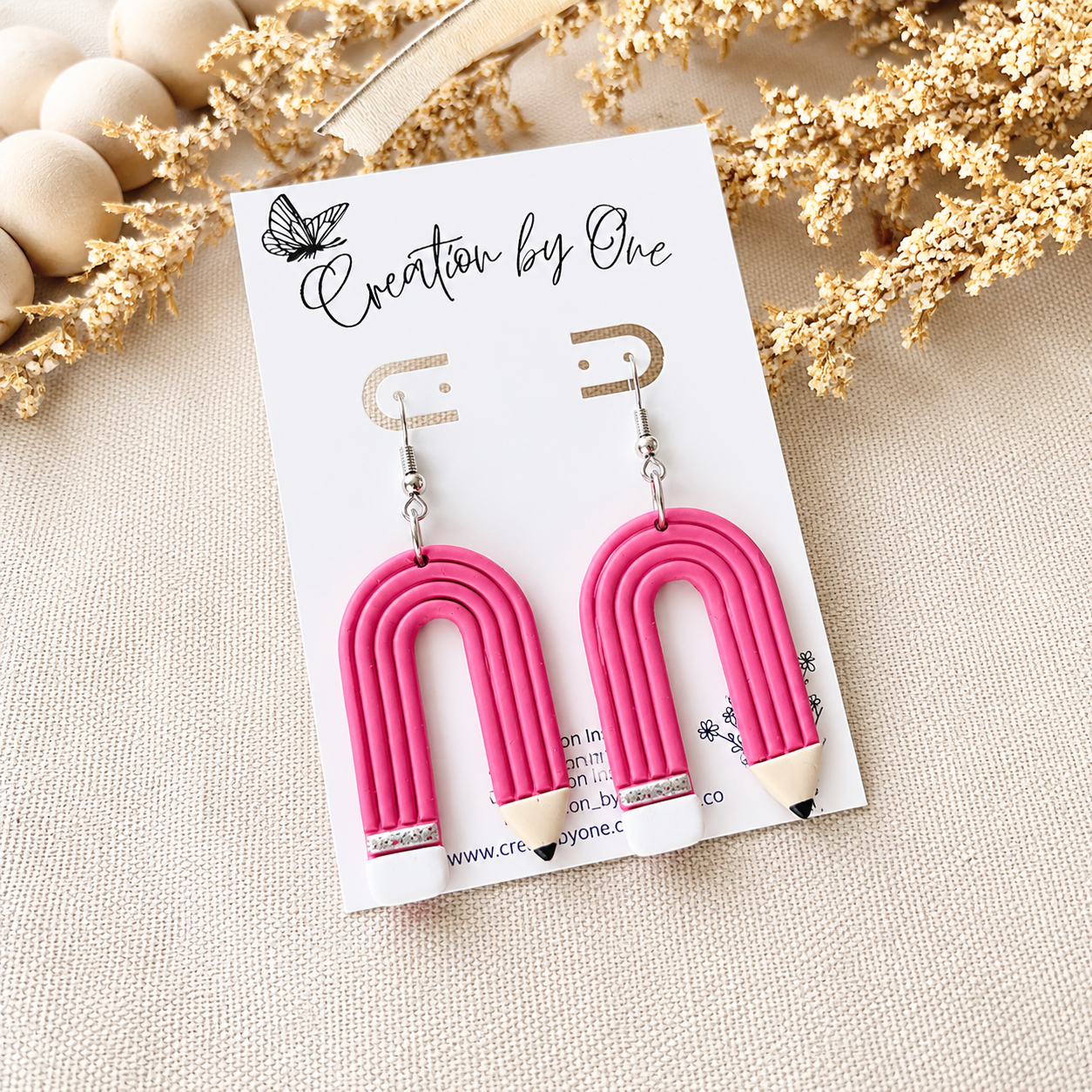 Pink arch-shaped earrings on a 'Creation by One' branded card with decorative elements.