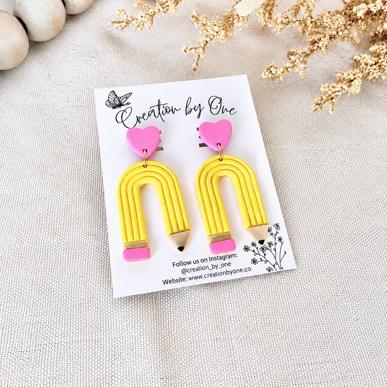 Yellow U-shaped earrings with pink accents on a 'Creation by One' branded card.
