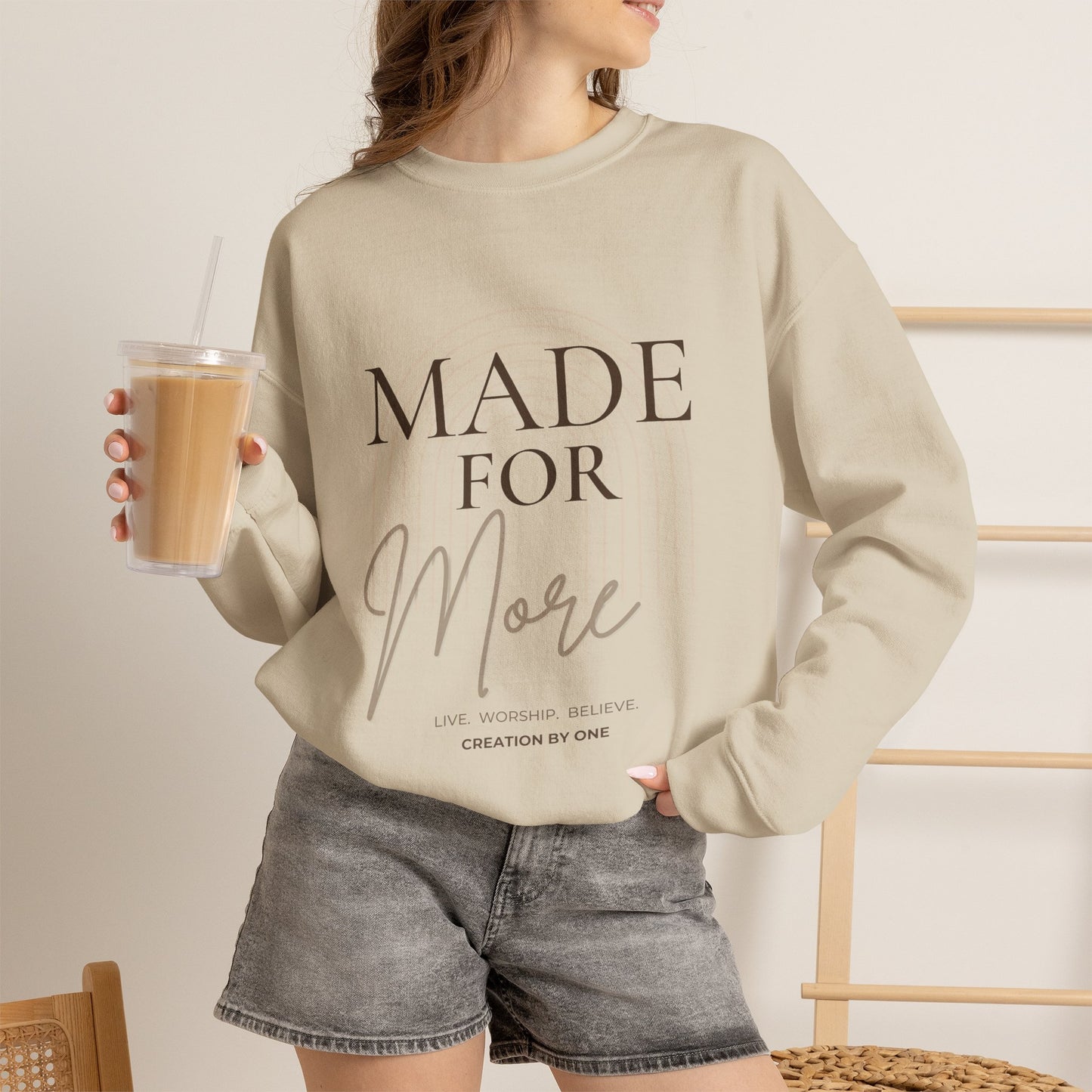 Person wearing a beige sweatshirt with 'MADE FOR MORE' text, holding a drink.