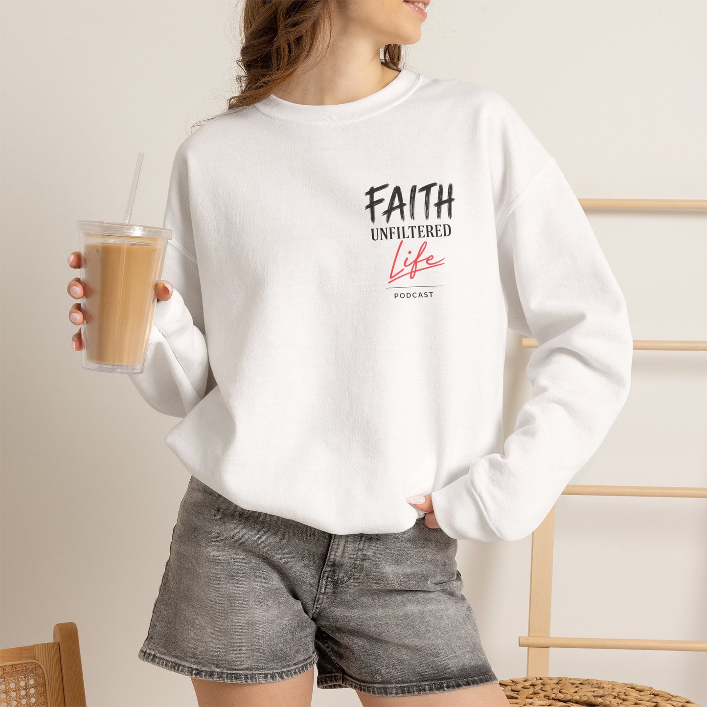 Person wearing a white sweatshirt with a logo, holding a drink, on a neutral background