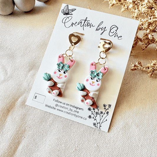 Pair of rabbit-shaped earrings on a 'Creation by One' branded card with decorative elements.