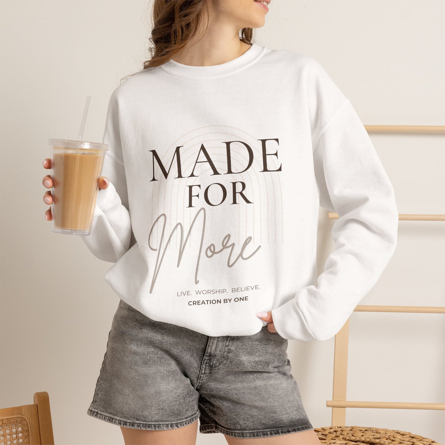 Person wearing a white sweatshirt with text, holding a drink.