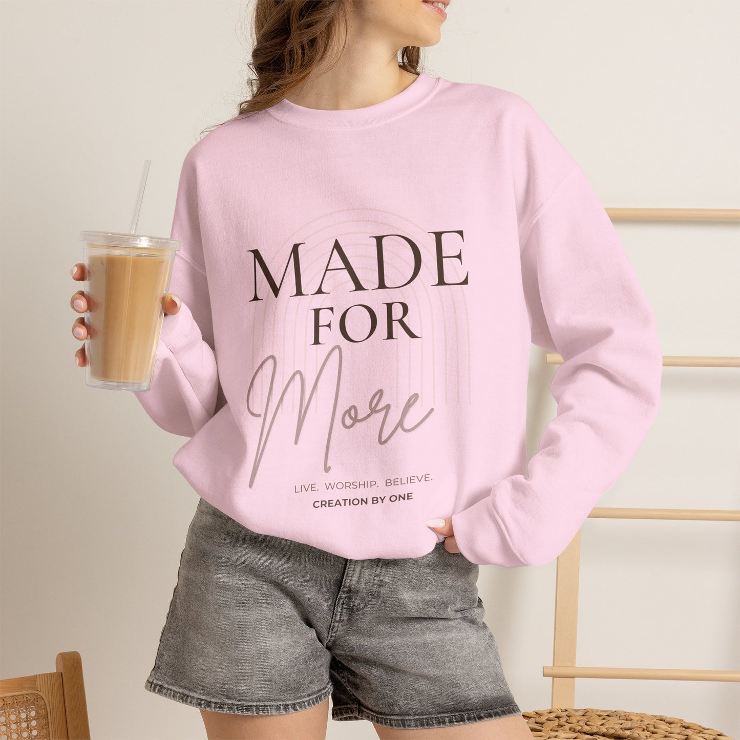Person wearing a pink sweatshirt with text, holding a drink.