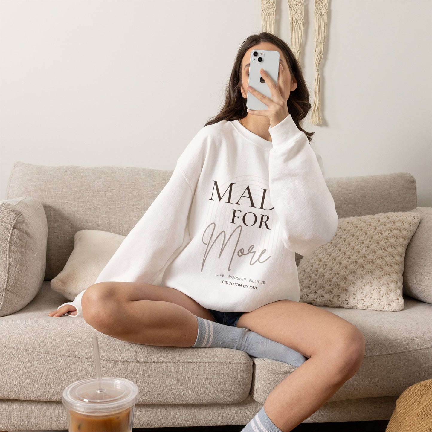 Person sitting on a couch wearing a white sweatshirt with text, holding a phone.