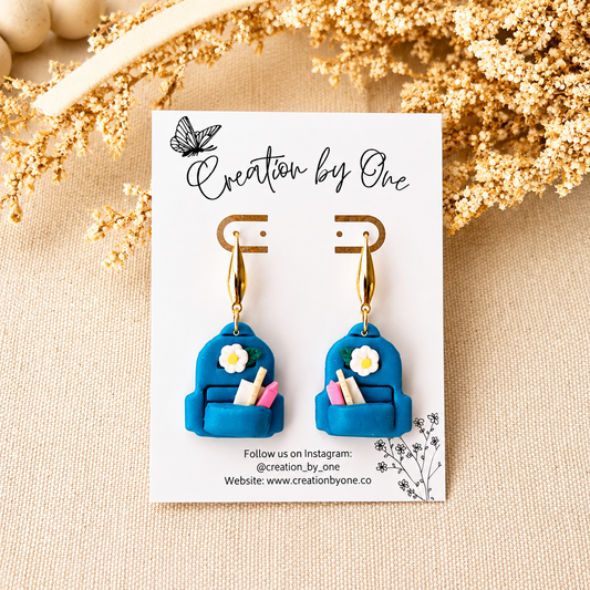 Blue earrings with floral details on a branded card against a beige background