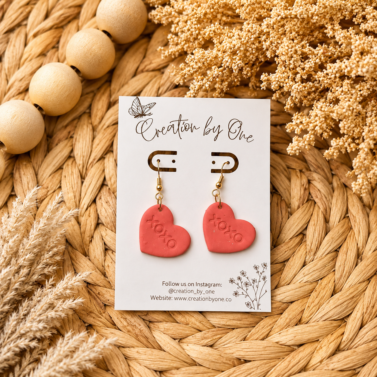 Red heart-shaped earrings on a 'Creation by One' branded card with decorative elements.
