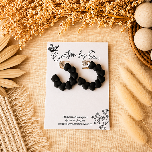 Black hoop earrings on a 'Creation by One' branded card with decorative elements on a beige background