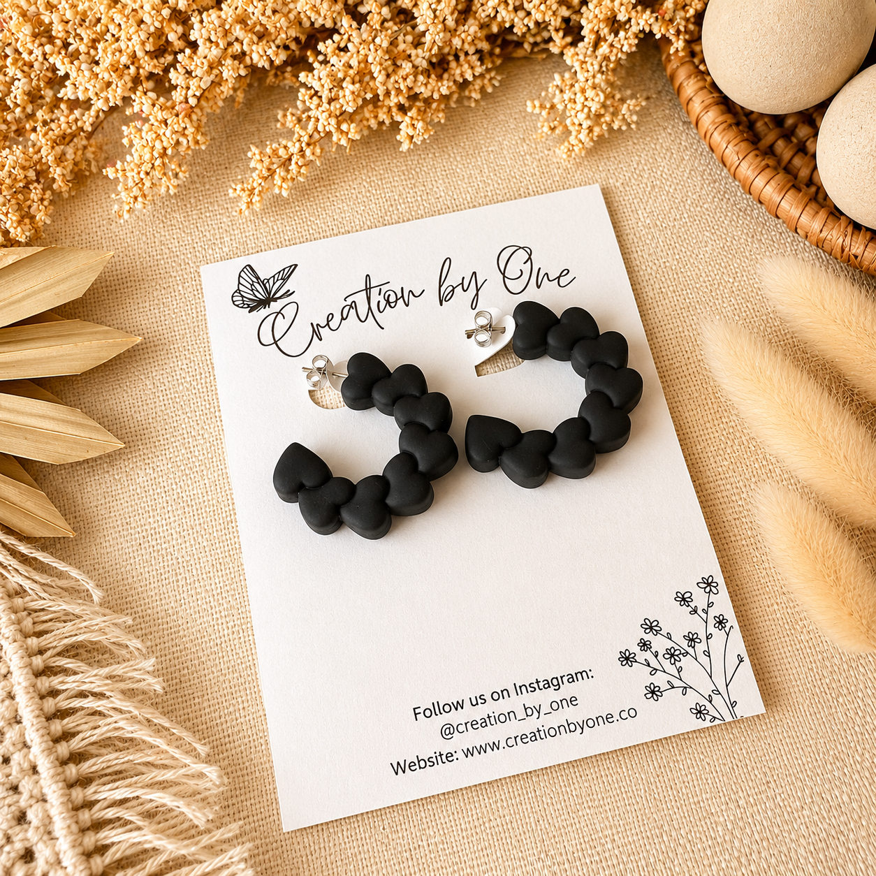 Black heart-shaped earrings on a branded card with decorative elements on a beige surface.