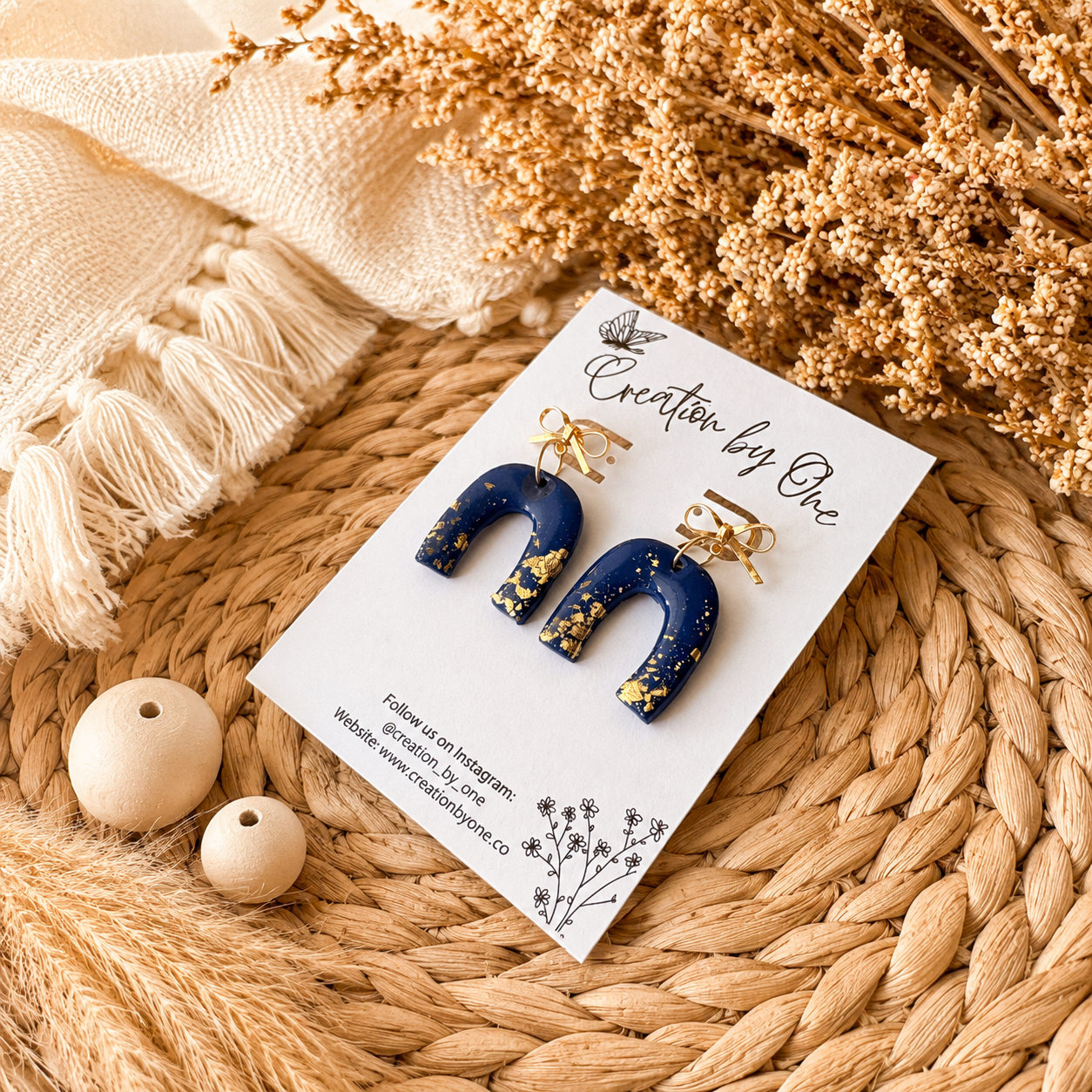 Navy blue earrings with gold accents on a branded card, placed on a woven surface with decorative elements.