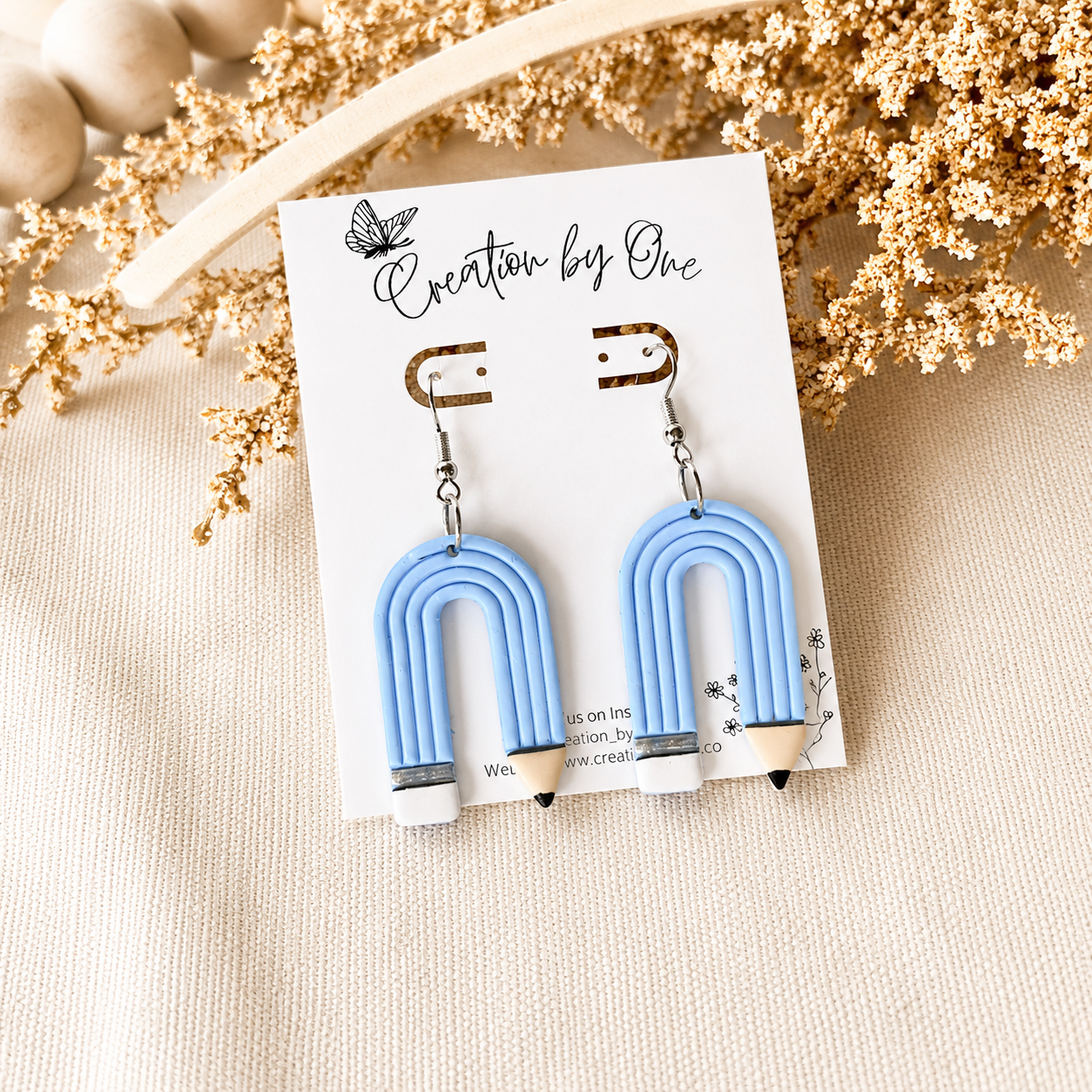 Blue U-shaped earrings on a 'Creation by One' branded card with decorative elements.