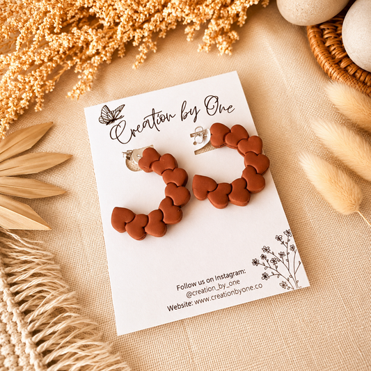 Heart-shaped earrings on a branded card with decorative elements on a beige surface