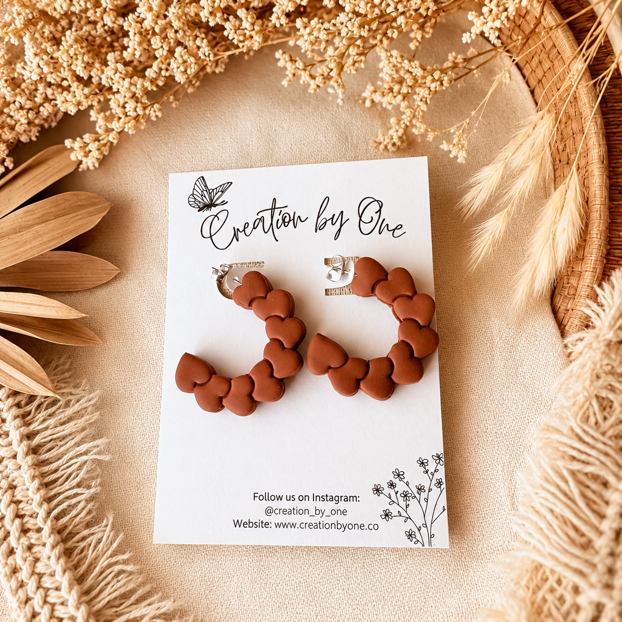 Brown heart-shaped earrings on a 'Creation by One' branded card with decorative elements.