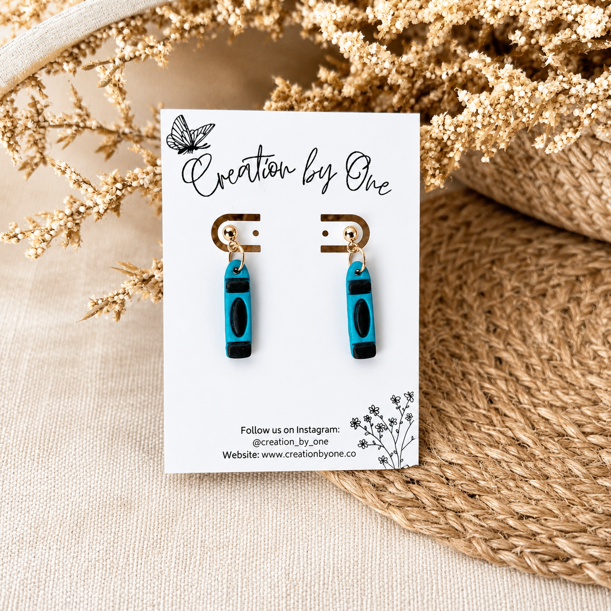 Pair of earrings on a 'Creation by One' branded card with decorative elements.