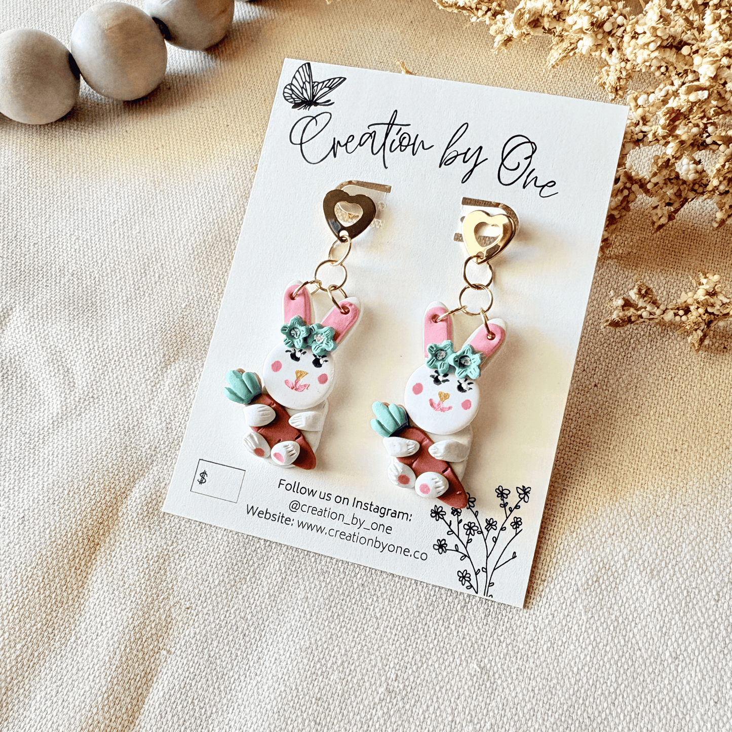 Pair of bunny-shaped earrings on a 'Creation by One' branded card with decorative elements.