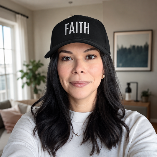 Woman wearing a black cap with 'FAITH' on it in a room with a couch and plant.