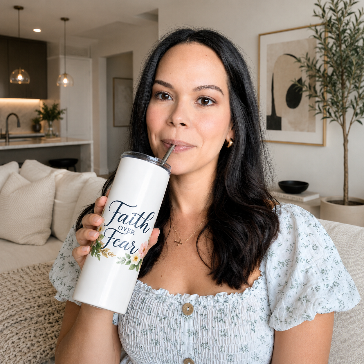 Woman holding a white tumbler with 'Faith over Fear' text in a living room.