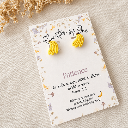 Yellow banana-shaped earrings on a 'Creation by One' branded card with decorative elements.