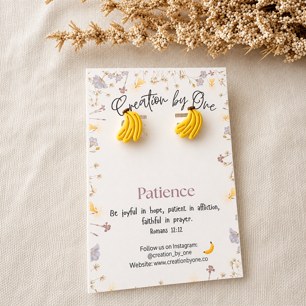 Banana-shaped earrings on a 'Creation by One' branded card with decorative elements.