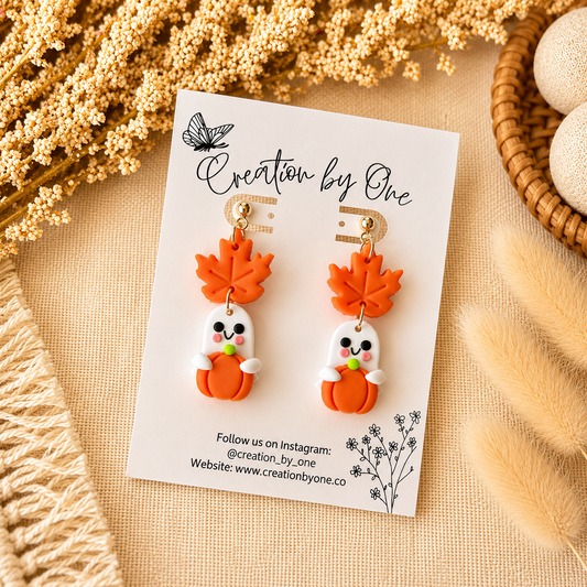 Pair of ghost-shaped earrings with orange leaves on a 'Creation by One' branded card, surrounded by decorative elements.