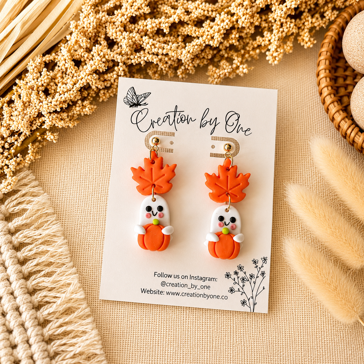 Pair of orange leaf-shaped earrings on a 'Creation by One' branded card with decorative elements.