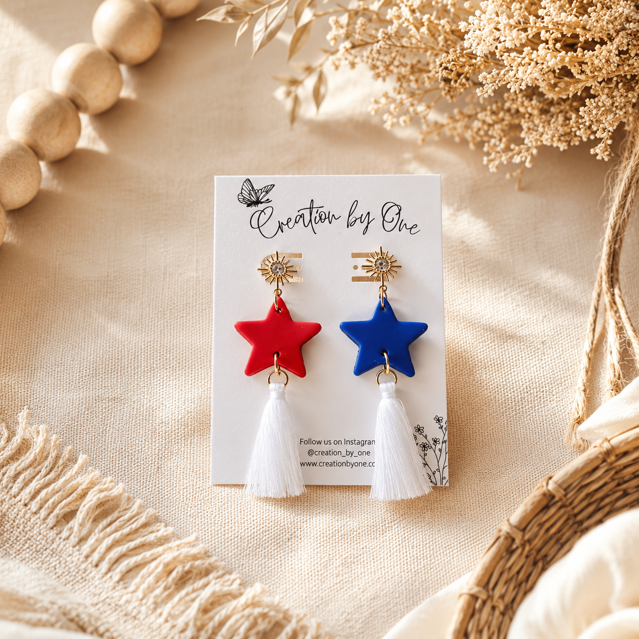 Star-shaped earrings with tassels on a 'Creation by One' branded card, surrounded by natural elements.