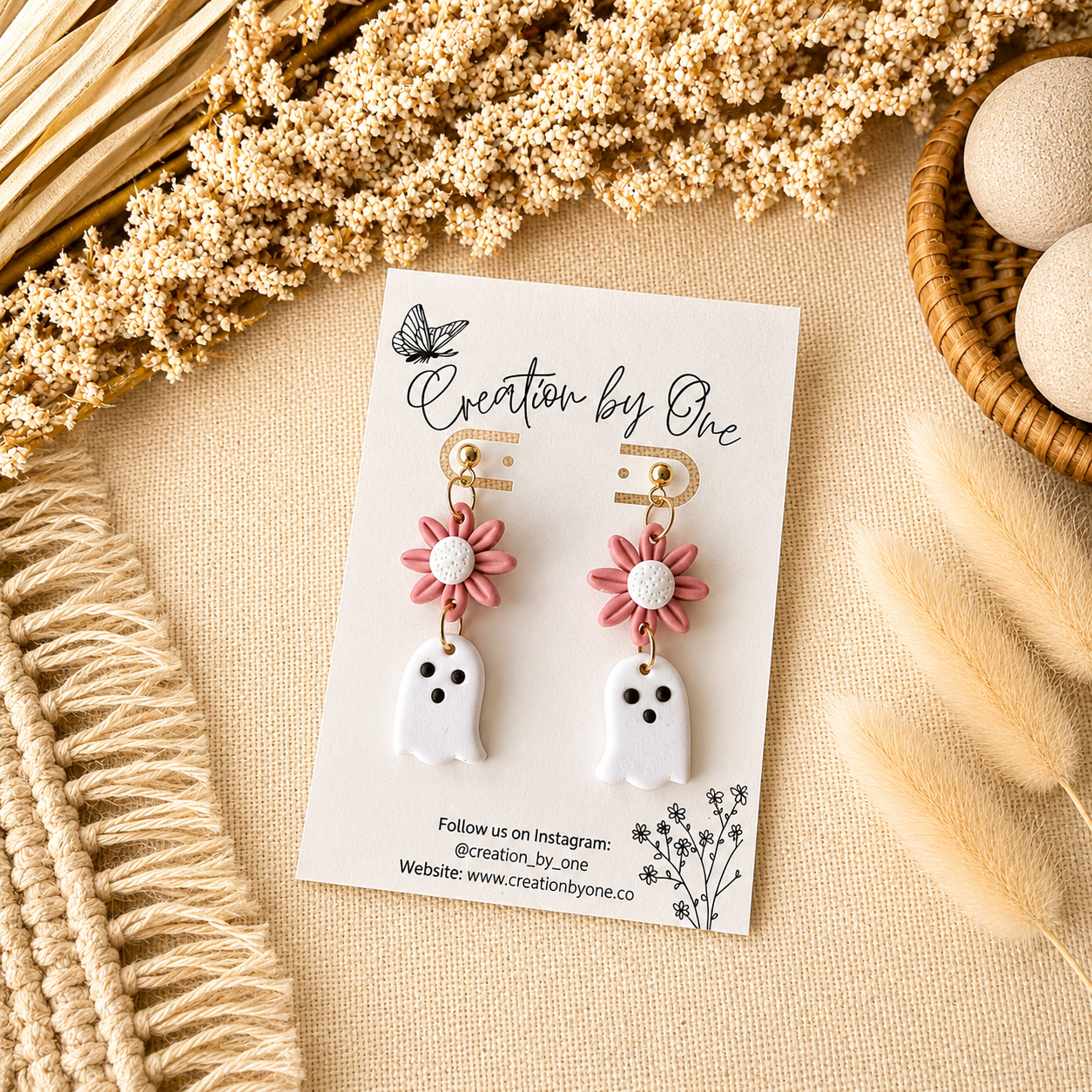 Pair of ghost-shaped earrings with pink flower details on a 'Creation by One' branded card, surrounded by decorative elements.