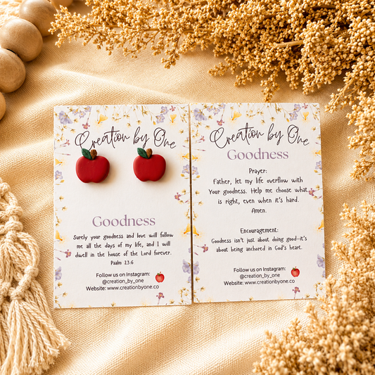Card with red apple earrings and text on a beige fabric background