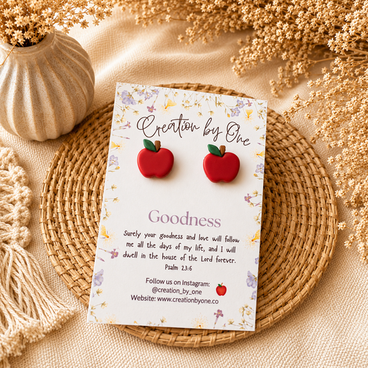 Red apple-shaped earrings on a 'Creation by One' branded card with decorative elements.