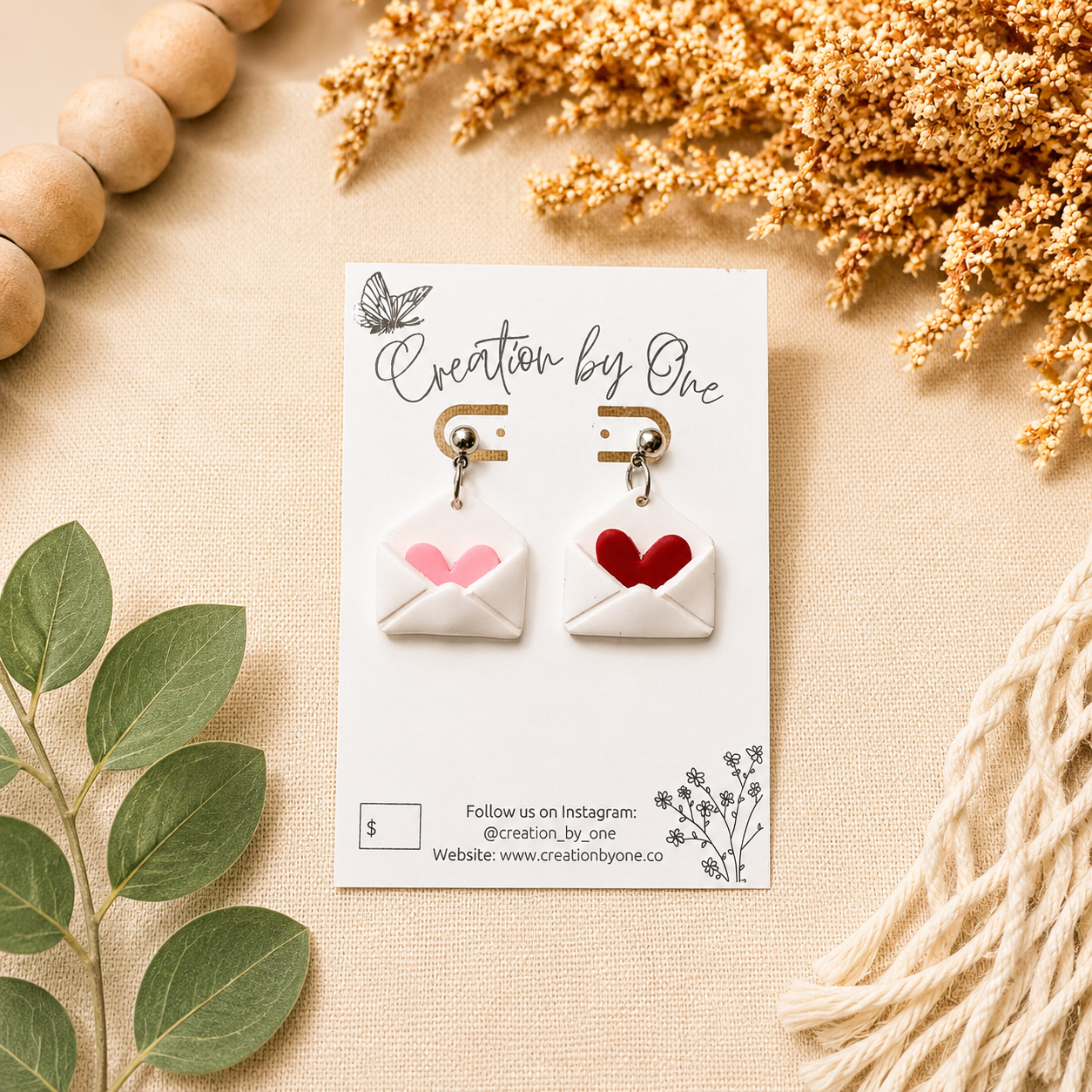 Handmade envelope heart dangle earrings displayed on a Creation by One jewelry card, styled on a neutral linen background with dried florals and natural wood beads in a modern boho flat lay. Perfect Valentine’s Day gift jewelry.