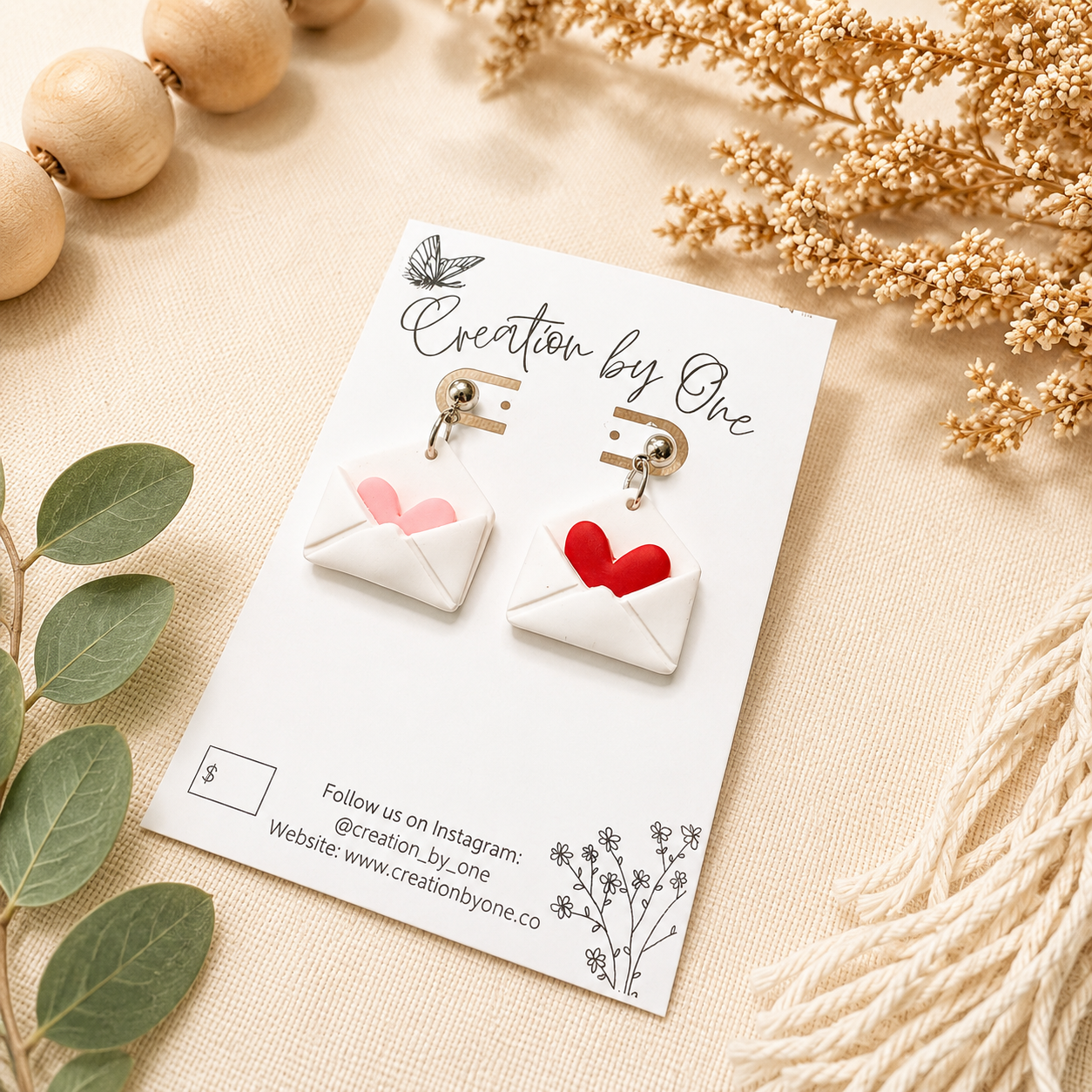 Handmade envelope heart dangle earrings displayed on a Creation by One jewelry card, styled on a neutral linen background with dried florals and natural wood beads in a modern boho flat lay. Perfect Valentine’s Day gift jewelry.