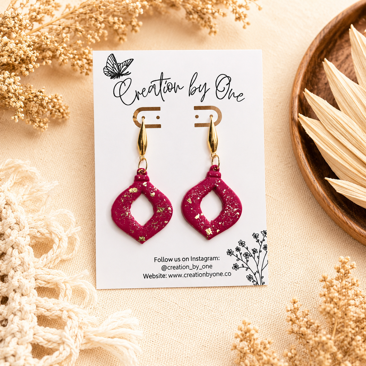 Handmade hot pink polymer clay dangle earrings with gold leaf flakes and gold-tone teardrop studs, displayed on a Creation by One jewelry card against a neutral boho linen background with dried florals.