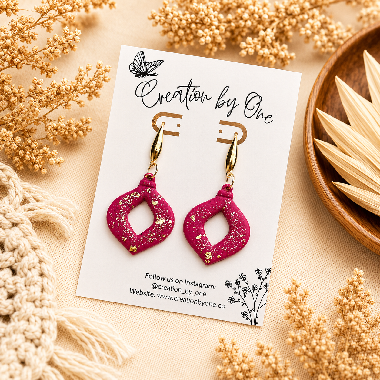 Handmade hot pink polymer clay dangle earrings with gold leaf flakes and gold-tone teardrop studs, displayed on a Creation by One jewelry card against a neutral boho linen background with dried florals.