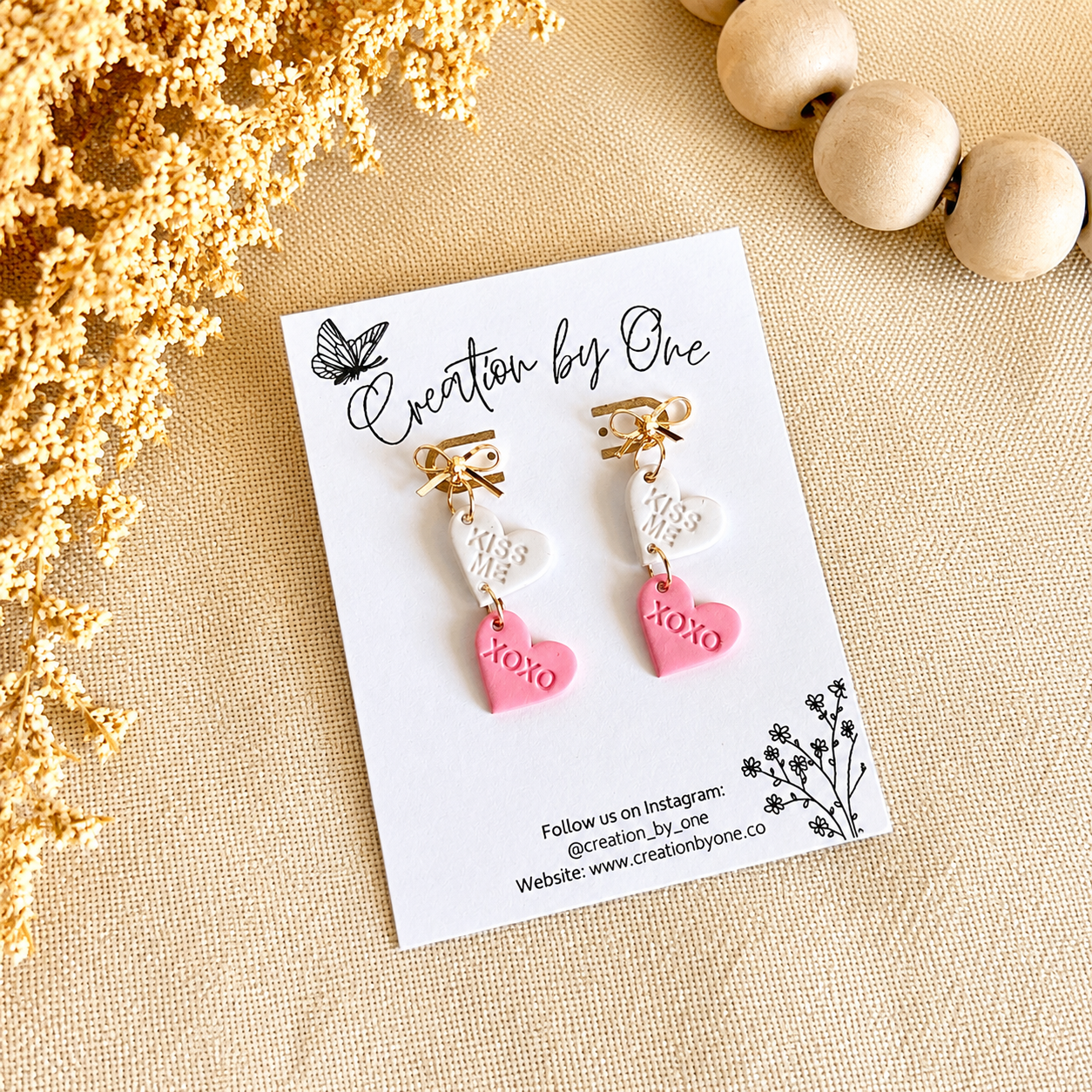 Heart-shaped earrings on a 'Creation by One' branded card with decorative elements.
