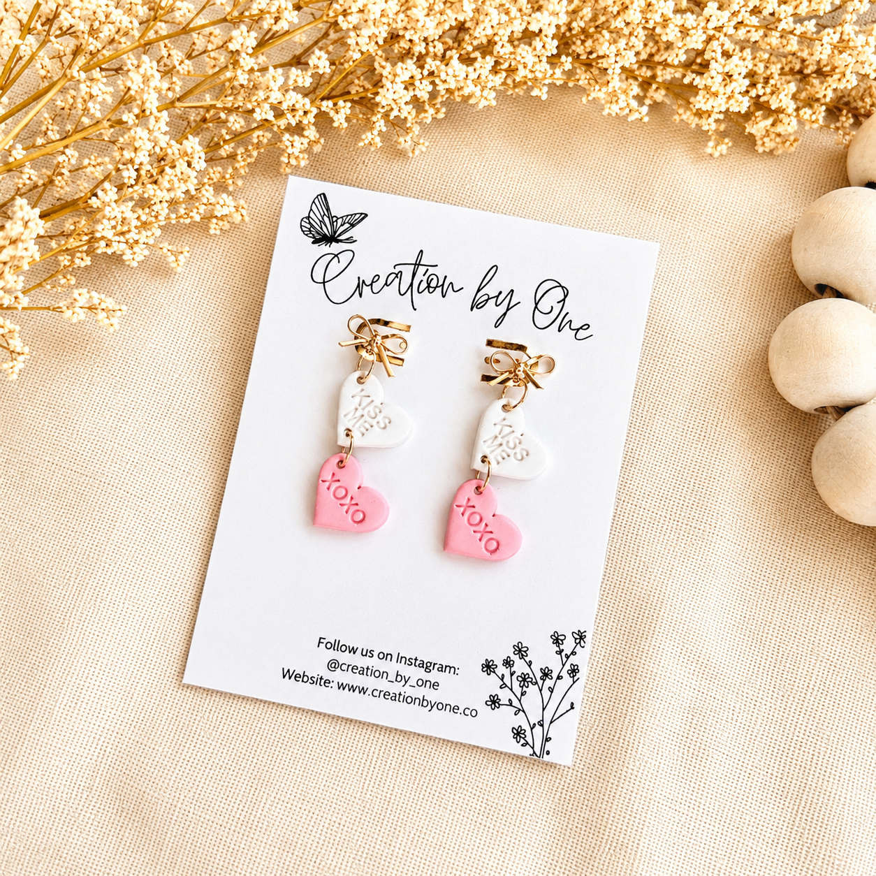 Pair of earrings on a 'Creation by One' branded card with decorative elements.