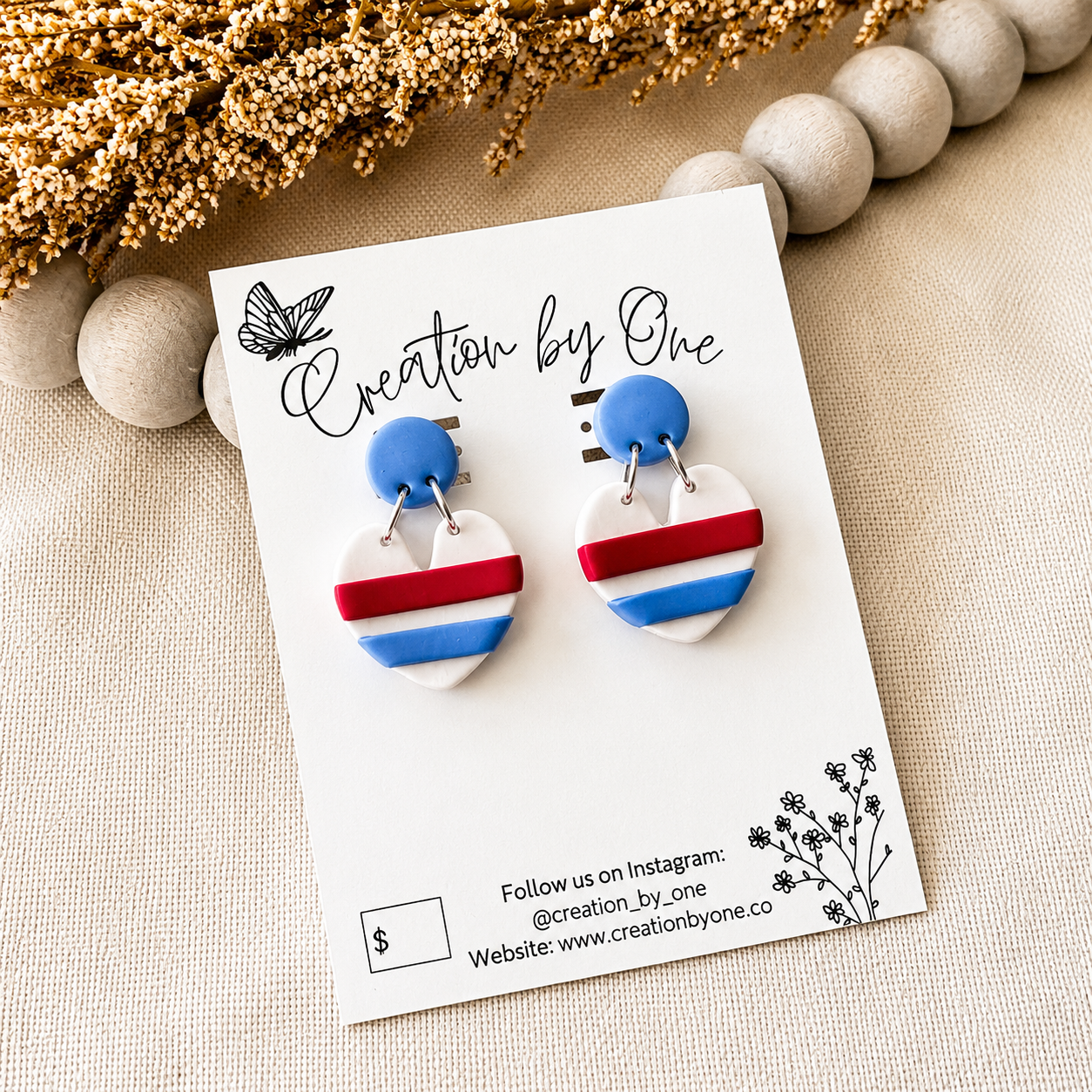 Pair of earrings on a 'Creation by One' branded card with decorative elements.