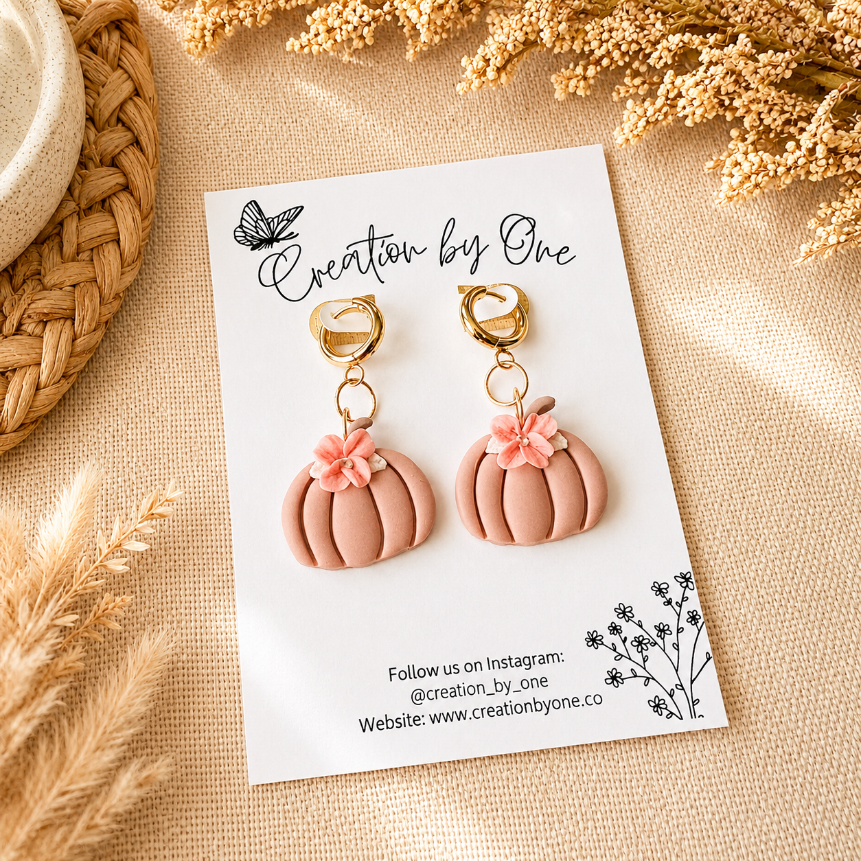 Pink pumpkin earrings with floral details on a 'Creation by One' branded card, surrounded by decorative elements.