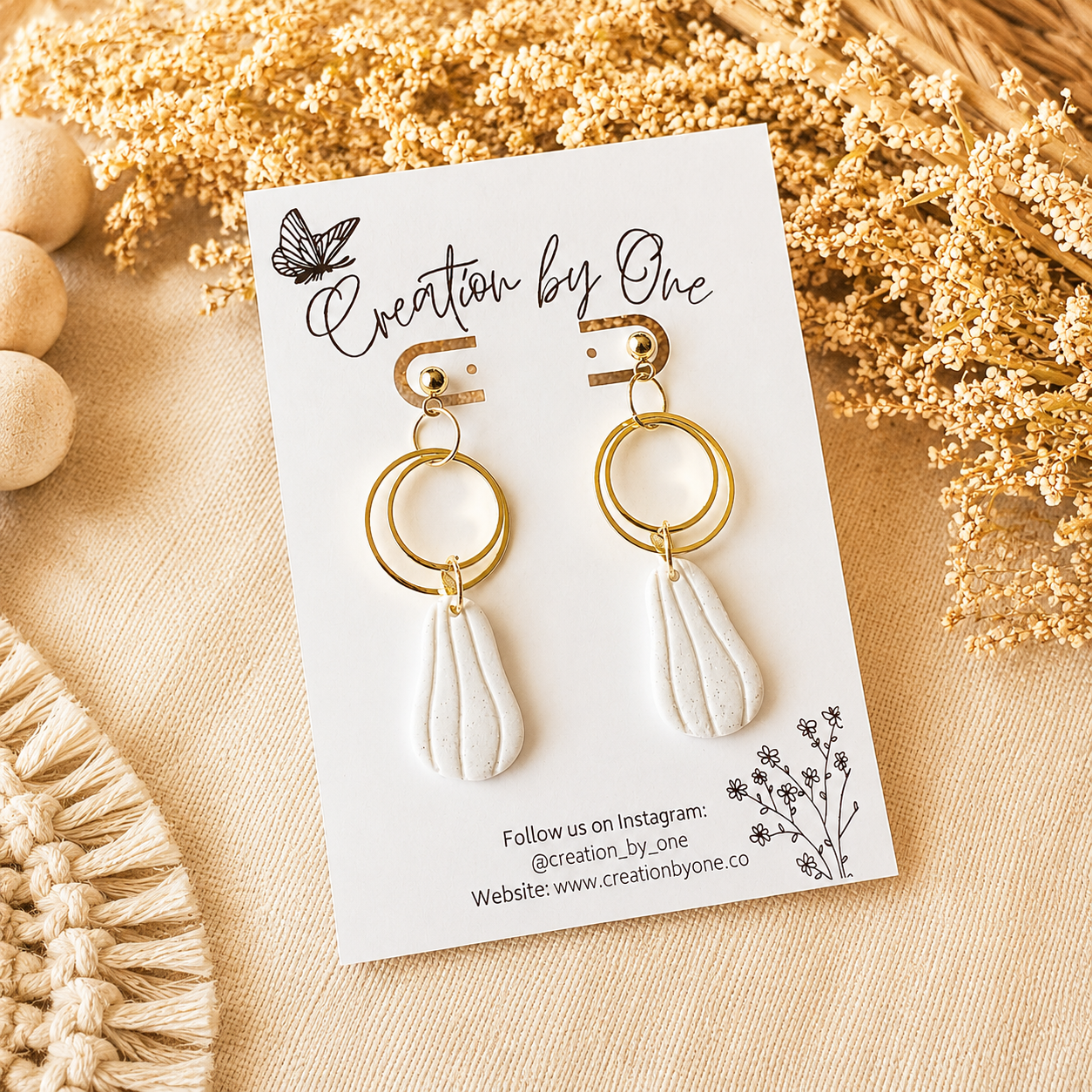 Gold and white earrings on a 'Creation by One' branded card with decorative elements.