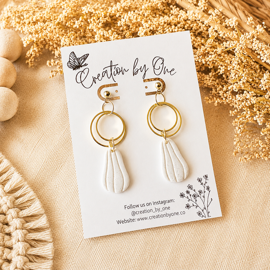 Gold and white earrings on a 'Creation by One' branded card with decorative elements.