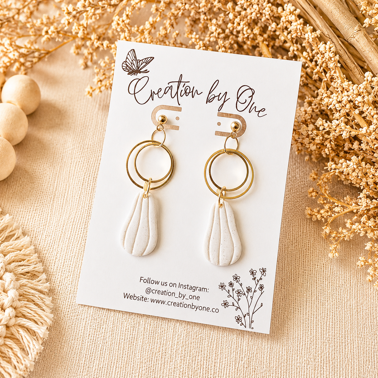 Gold and white earrings on a 'Creation by One' branded card with decorative elements.