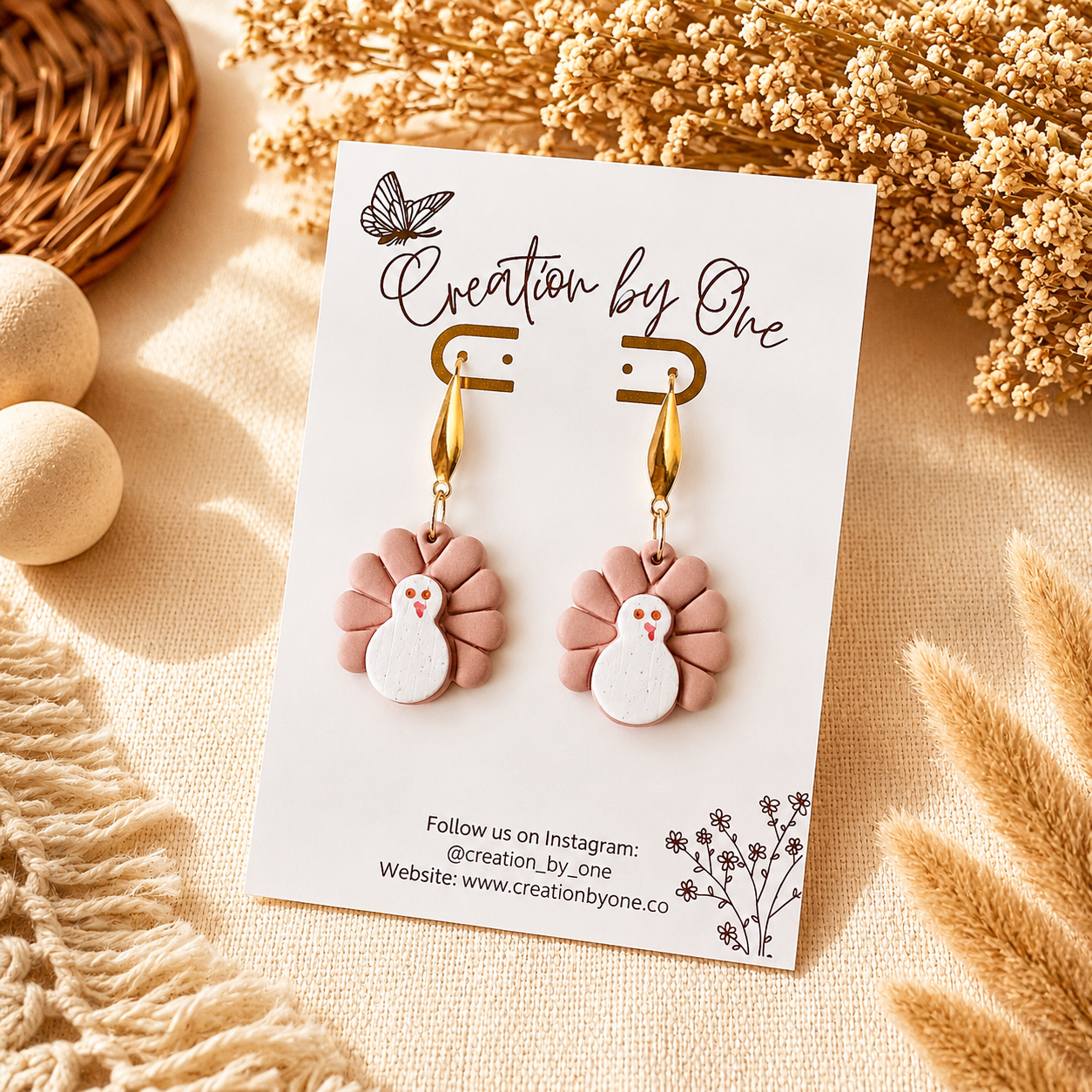 Pair of earrings on a 'Creation by One' branded card with decorative elements in the background.