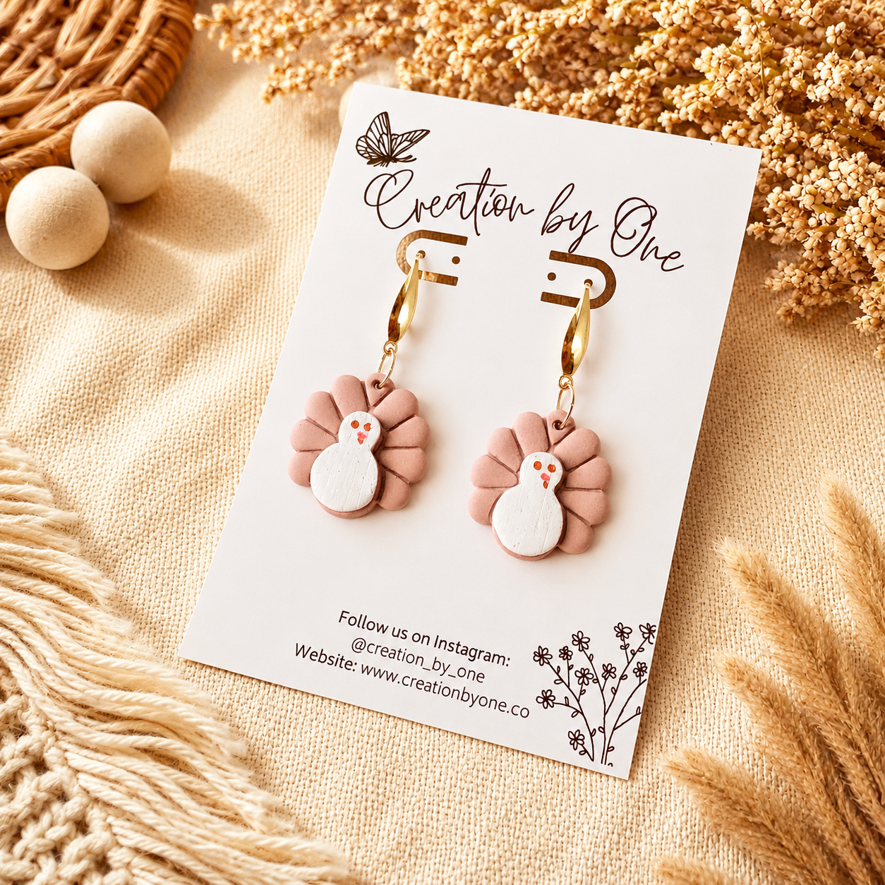 Pair of earrings on a 'Creation by One' branded card with decorative elements.