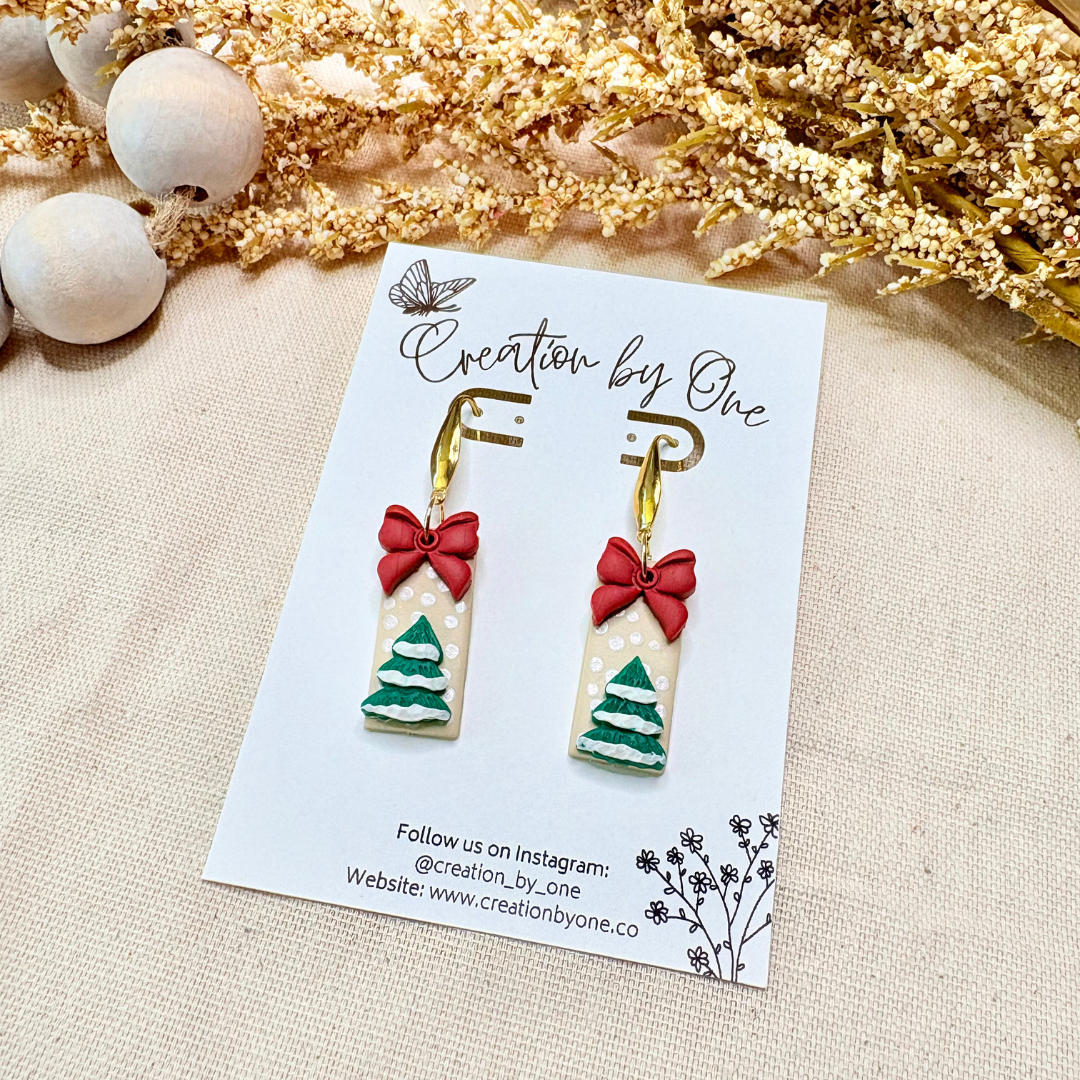 Neutral holiday bow earrings made from polymer clay with 14K gold-plated posts on winter-themed backdrop