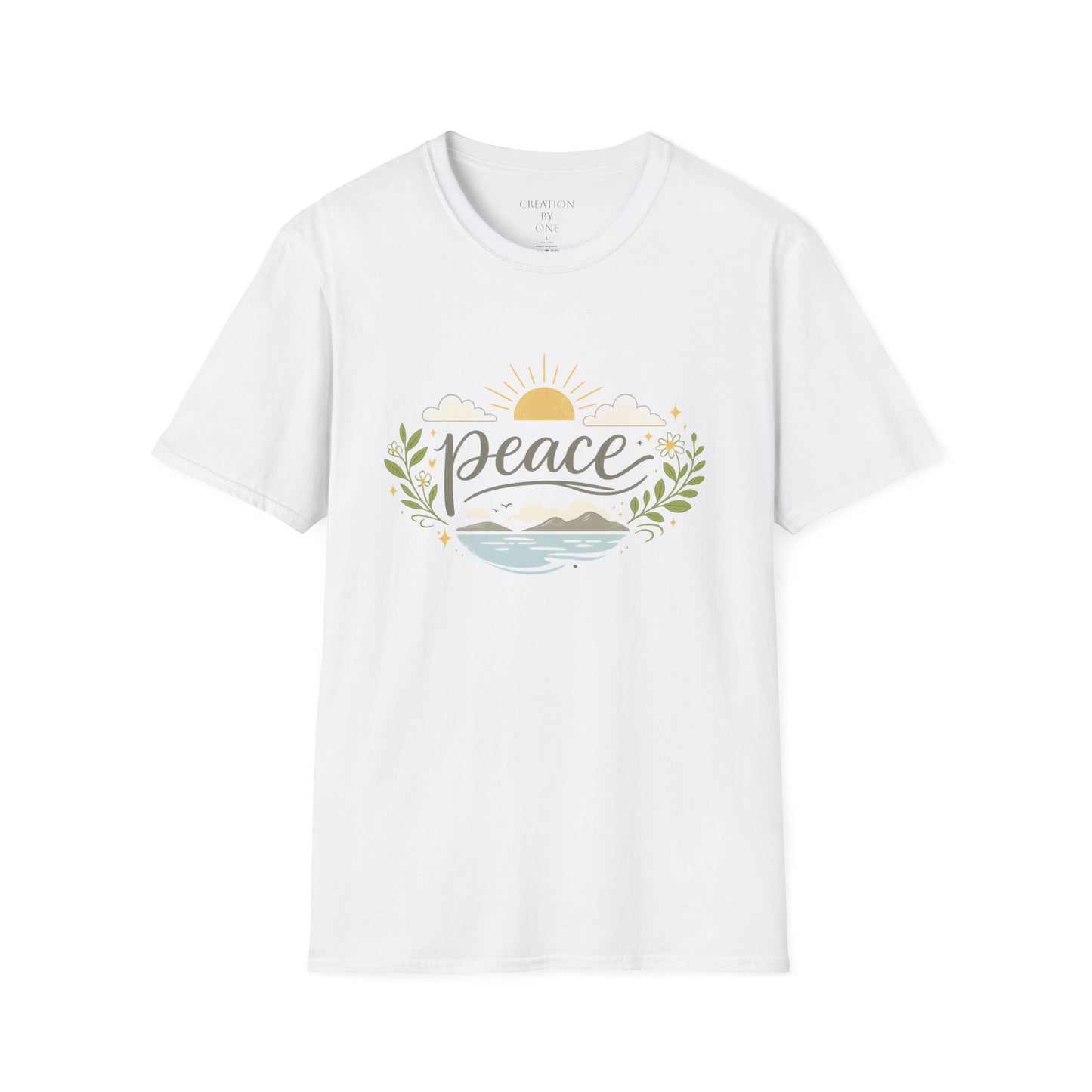A woman with long dark wavy hair wears a neutral sand-colored graphic T-shirt and a beige baseball cap in a bright modern boho setting. The T-shirt features the word "Peace" in elegant script above a tranquil landscape with a golden sunrise, soft clouds, mountains, blue water, leafy branches, and delicate floral accents. She pairs the shirt with blue jeans and a simple gold cross necklace, standing in front of neutral décor with eucalyptus, pampas grass, and cozy textured accents for a calm, faith-inspired 