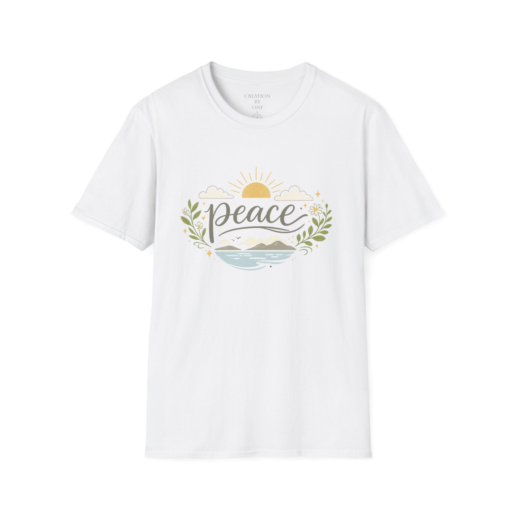 A woman with long dark wavy hair wears a neutral sand-colored graphic T-shirt and a beige baseball cap in a bright modern boho setting. The T-shirt features the word "Peace" in elegant script above a tranquil landscape with a golden sunrise, soft clouds, mountains, blue water, leafy branches, and delicate floral accents. She pairs the shirt with blue jeans and a simple gold cross necklace, standing in front of neutral décor with eucalyptus, pampas grass, and cozy textured accents for a calm, faith-inspired 