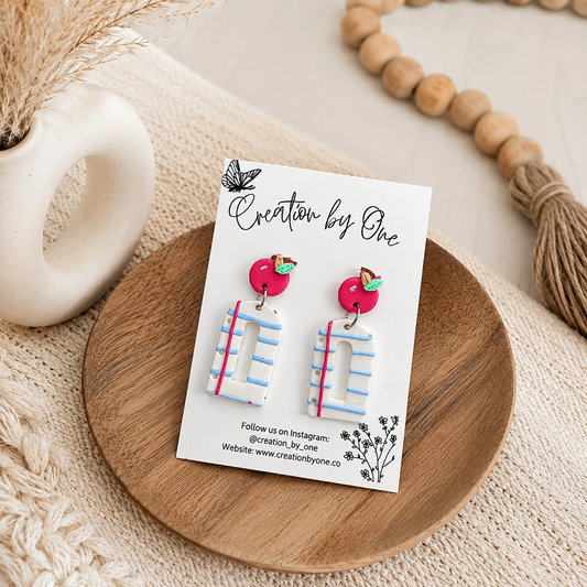 Earrings on a card labeled 'Creation by One' on a wooden surface.