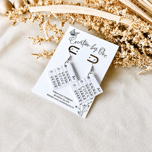 Pair of earrings on a 'Creation by One' branded card with dried flowers in the background.